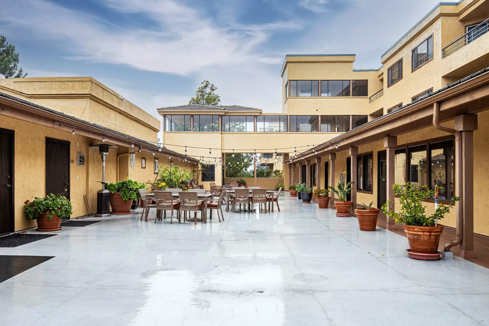 An exterior view of 3 tables with 11 chairs and two umbrellas outside of  a 55+ apartment senior living community